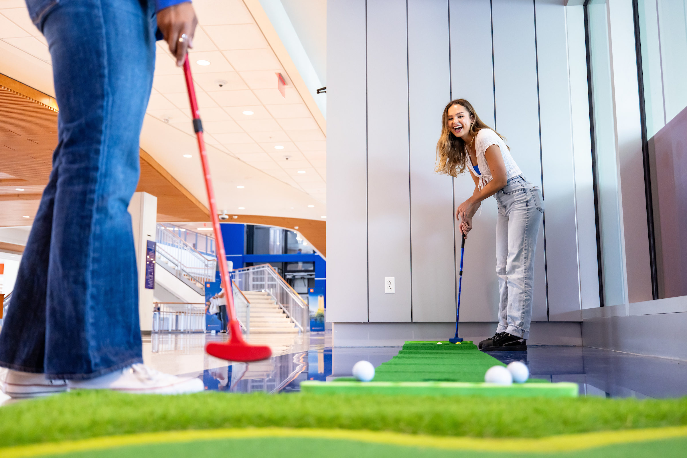 Two student put on the green inside of the Reitz Union and laugh.